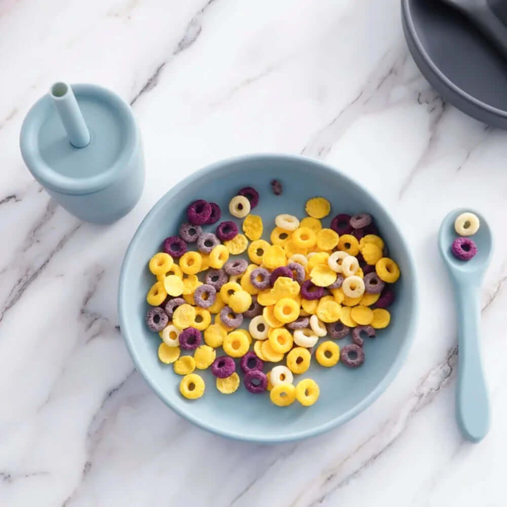 Children's tableware set in blue with the plate filled with cereal.